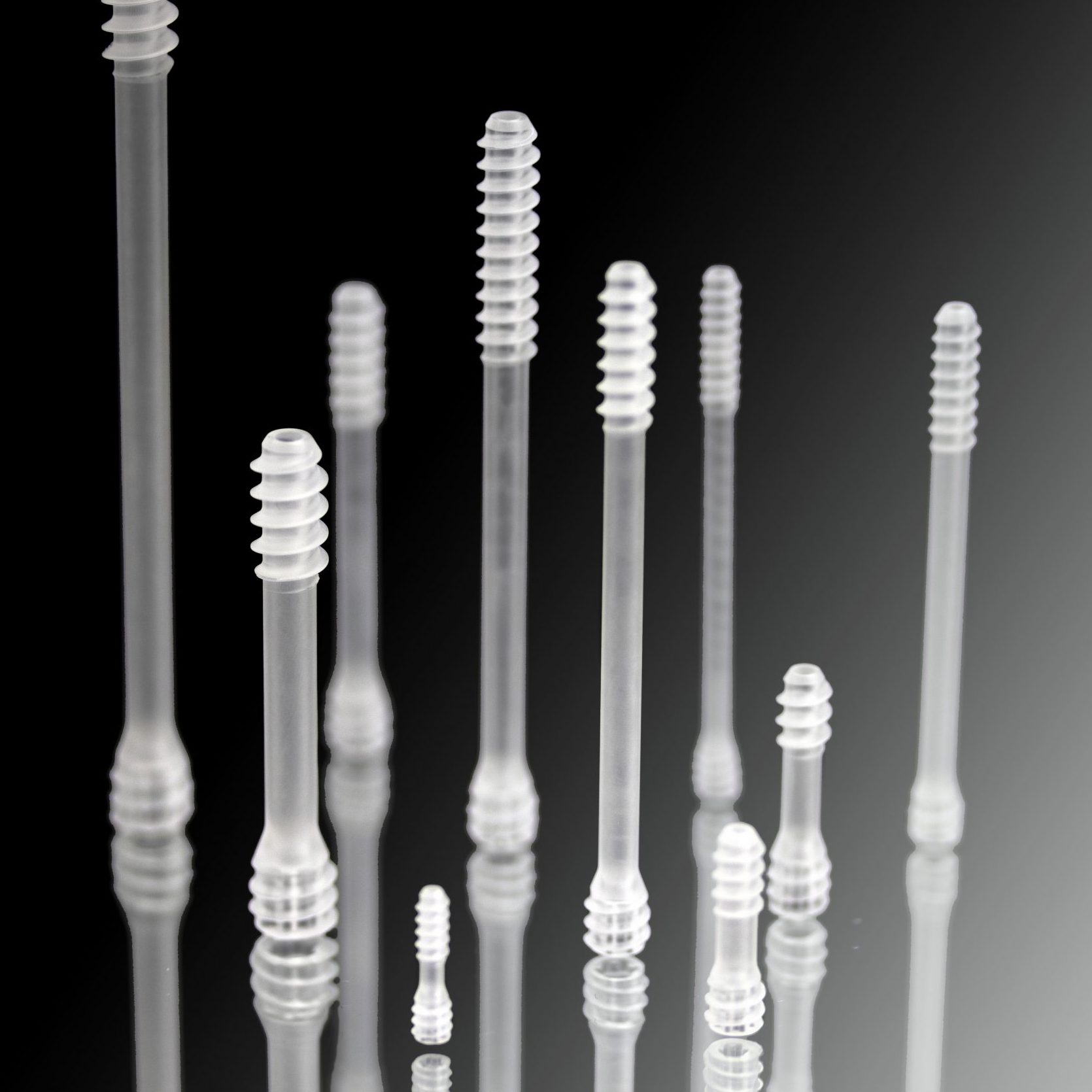 Black and white photo of bioabsorbable surgical screws in different sizes. The screws are placed on a mirror so their reflections are showing.