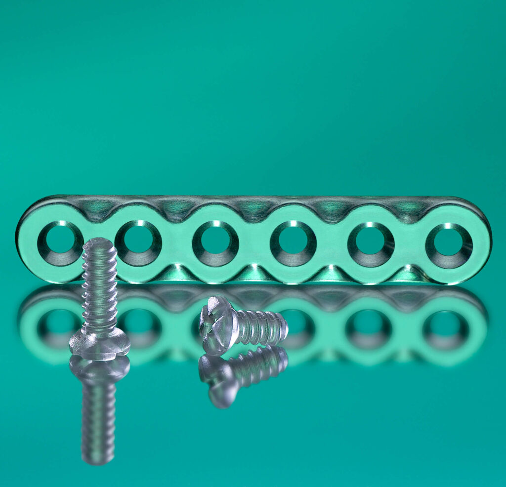 Inions CPS Bioabsorbable plate and Screws against a green background. The scerws and plate are placed on a mirror, so their reflection is showing.