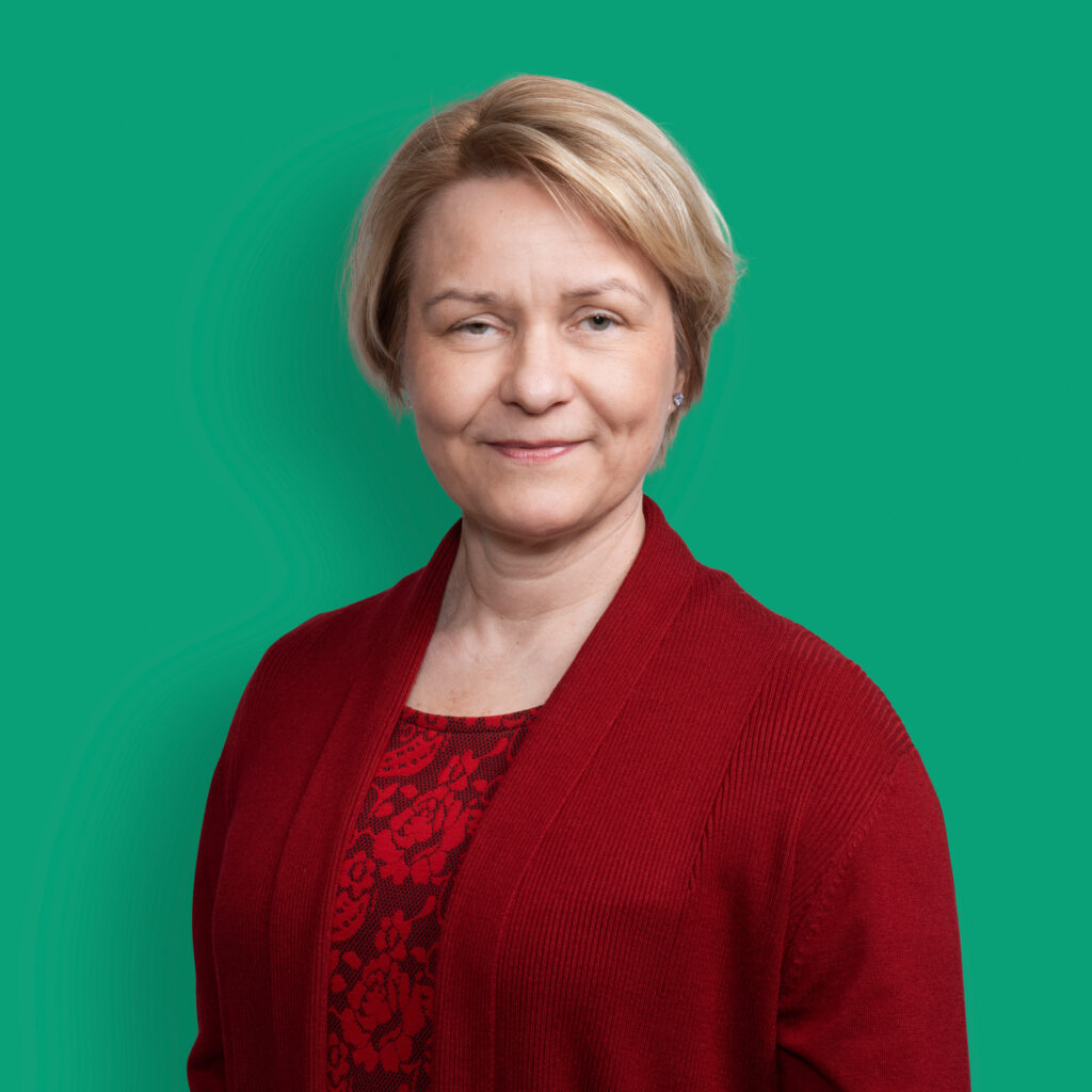 A portrait of a smiling person from the Inion management team wearing a red outfit green background. 